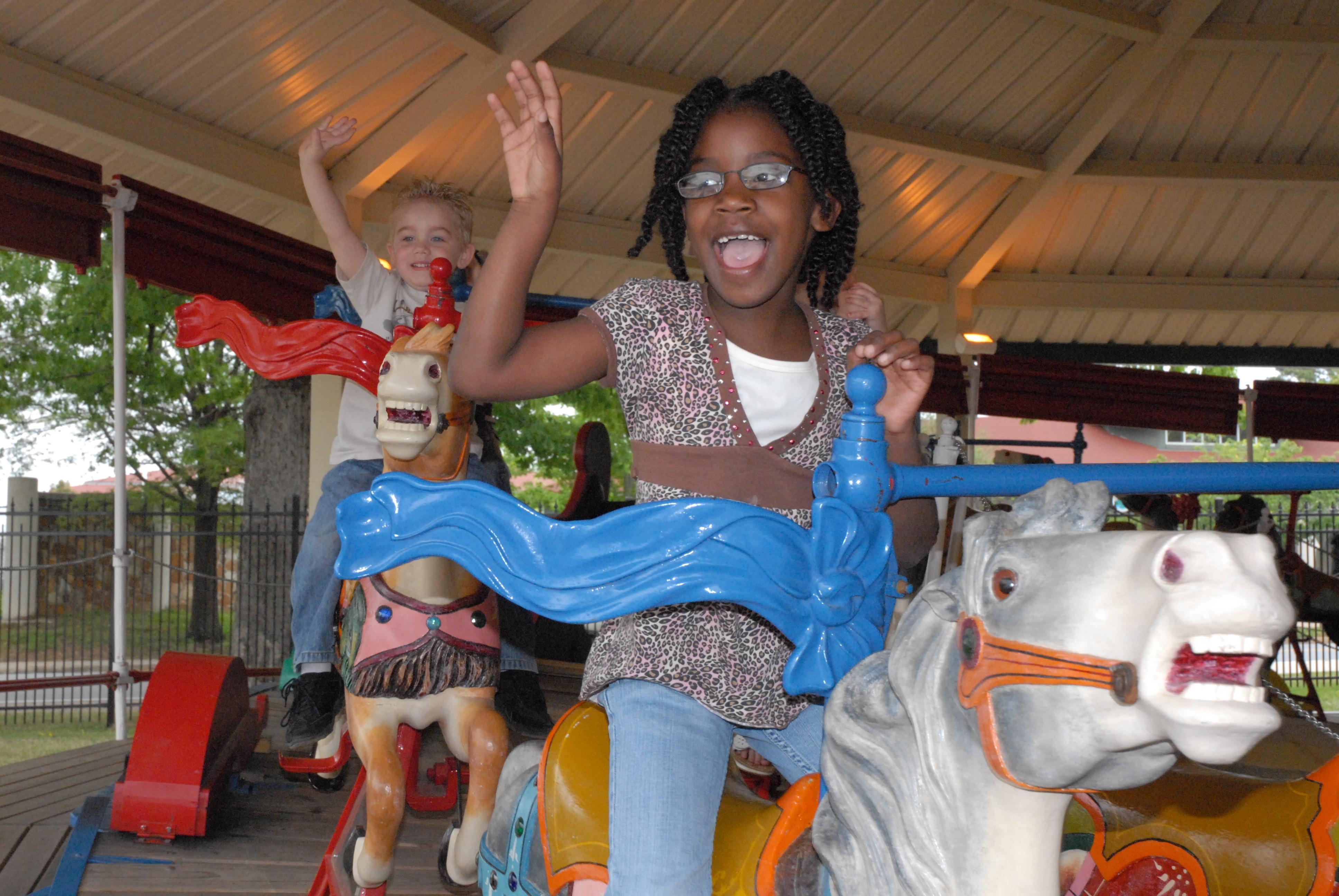 Two children laughing and waving as they ride the carousel at the Little Rock Zoo